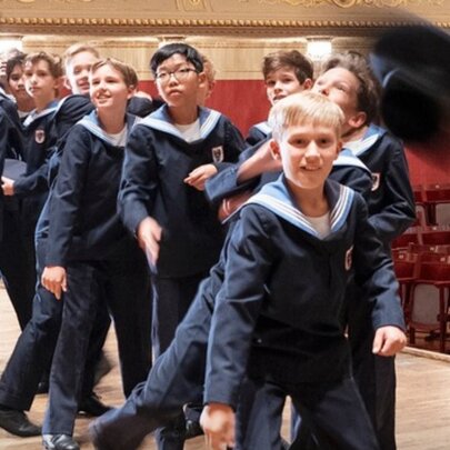 Young members of the Vienna Boys Choir wearing their signature sailor-suit uniforms in a large hall or performance space.