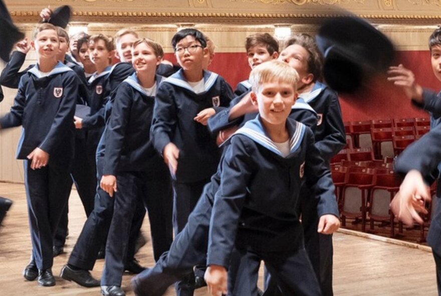 Young members of the Vienna Boys Choir wearing their signature sailor-suit uniforms in a large hall or performance space.