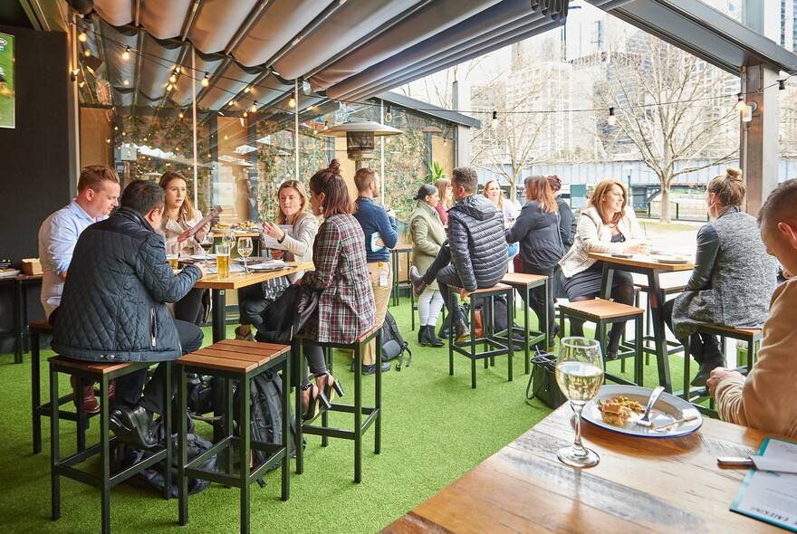 People seated at a riverside beer bar outside area, under cover.