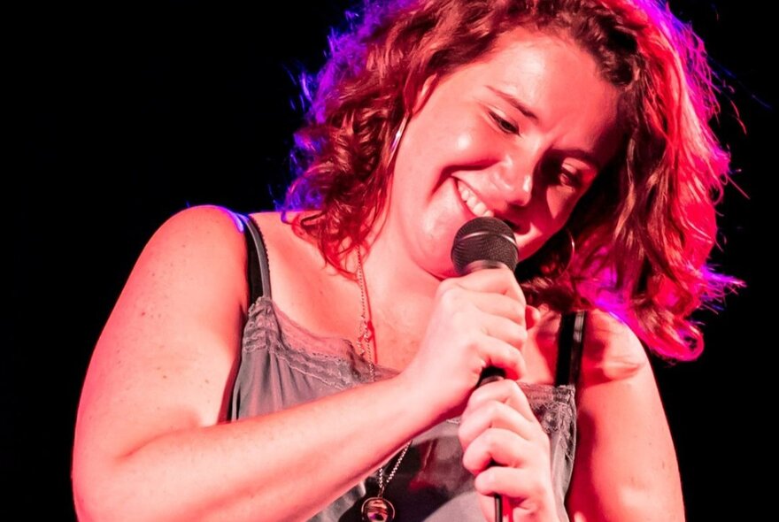 Woman performing with microphone on stage, smiling.