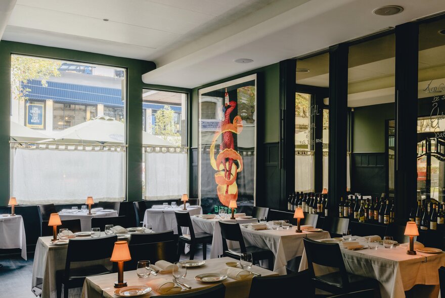 The dining room interior of Cafe Florentino restaurant on Bourke Street with tables covered in white linen and dark dining chairs, and small table lamps.