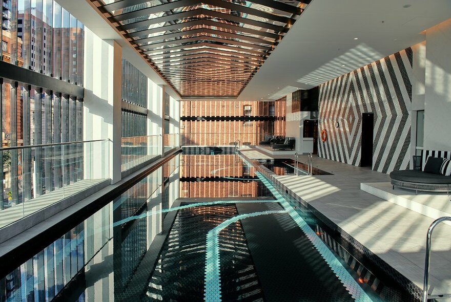 The indoor pool at Movenpick Hotel with glass windows all down the left side wall and patterned black and white tiles on the right side wall.