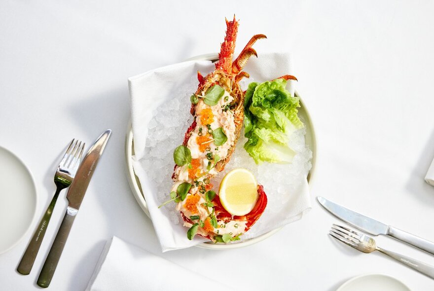White plate of seafood with halved crayfish and garnishes on a white table setting.