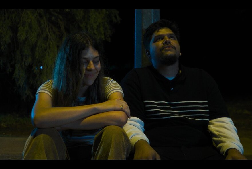 Still from the film Under Streetlights of two actors sitting side by side in relaxed seated poses.