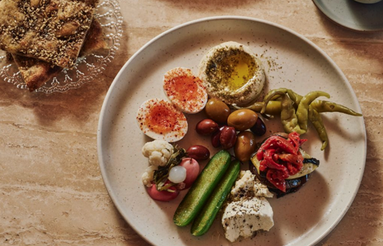 A breakfast plate with eggs, pickles, hummus and olives.