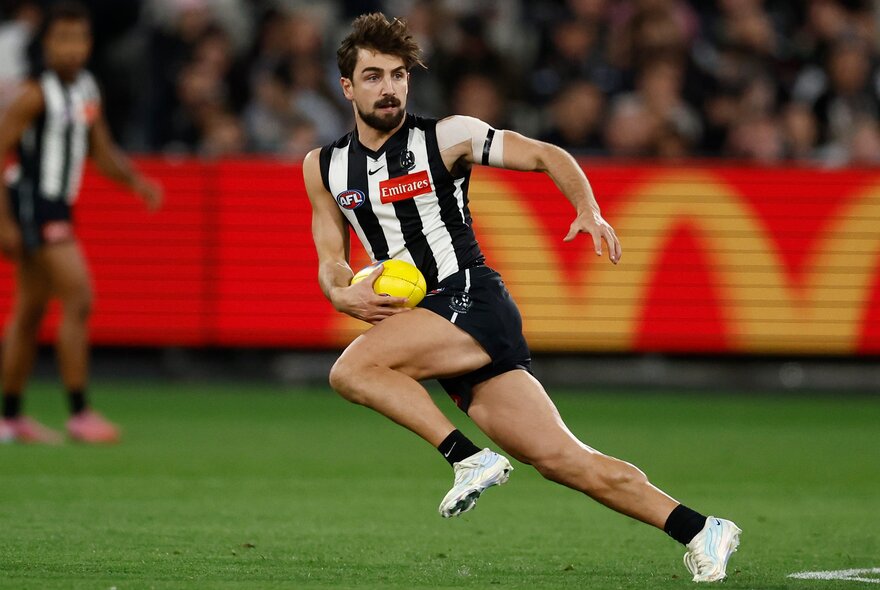 A Collingwood AFL football player running with the ball during a match.