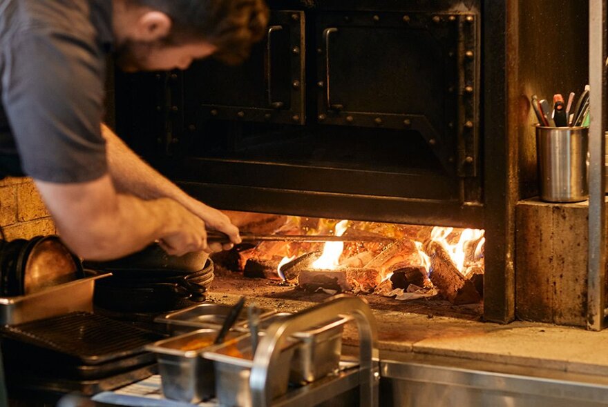 A chef tending to the wood in a large woodfire hearth in the kitchen of Aru restaurant.