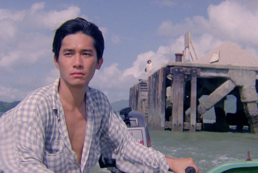 A still from an Asian movie showing a young man on a small boat with oil rig infrastructure behind him.