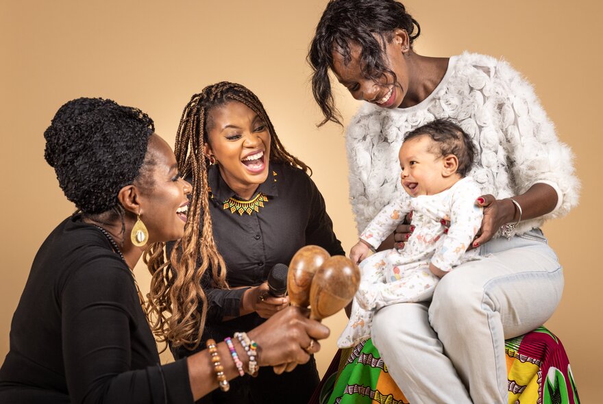 Three people interacting with a baby that is seated on a women's lap.