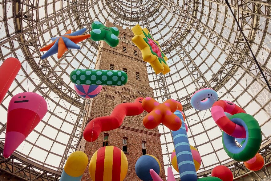 Inflatable colourful sculptures with faces hanging around a brick tower.