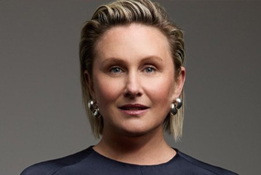 Woman with blonde-streaked hair swept back from forehead, with gold earrings.