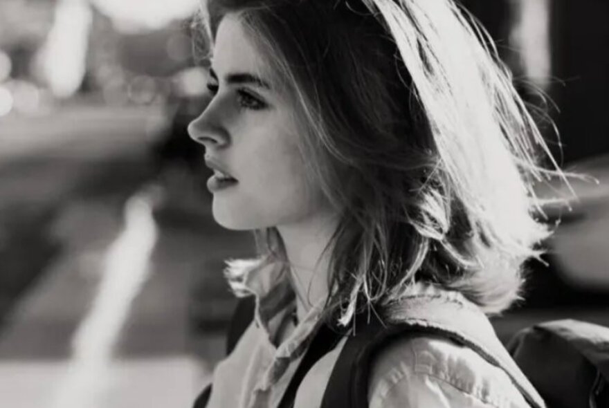 Black and white profile of singer Emmy Miller, a young woman with shoulder length hair, standing outside.