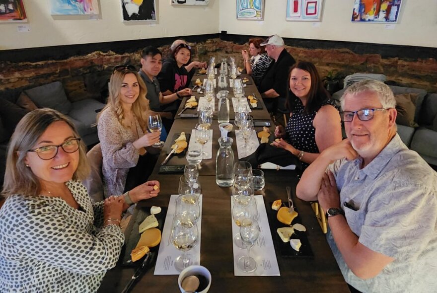 People seated at a long table set with glasses and cheese in a restaurant setting.