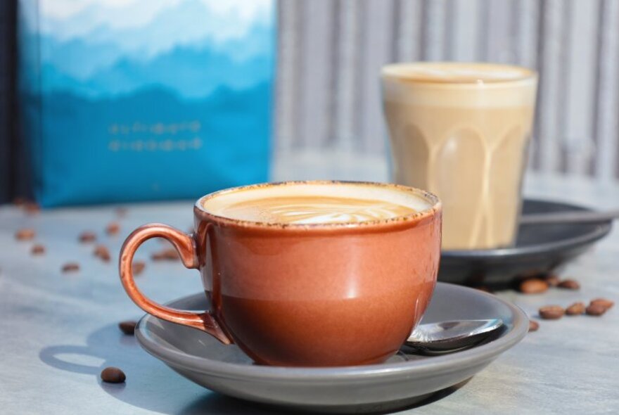 A cafe latte served in a glass and a flat white coffee in a cup, on a table.
