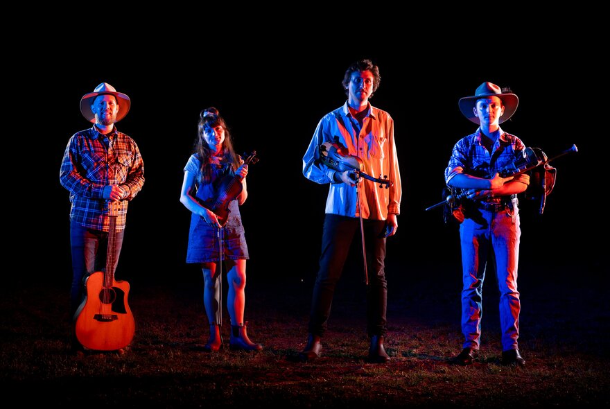 Four musicians holding guitars, lit by red and blue lights against a dark background.