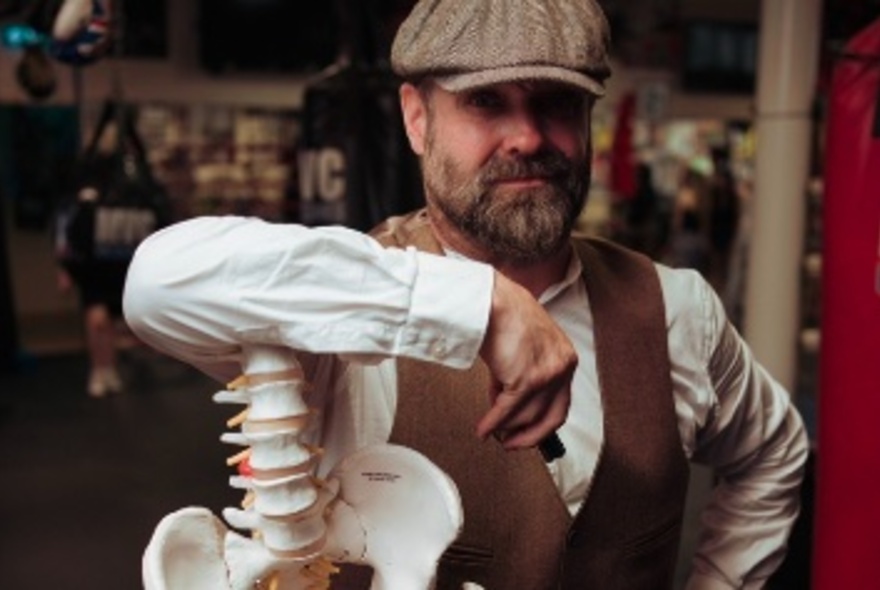 Author Roy Maloy wearing a cap with his arm resting on spine of a display skeleton.