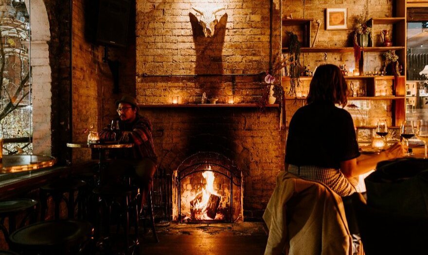 People sitting beside the fire in a cosy bar with brick walls and vintage trinkets on the shelves.