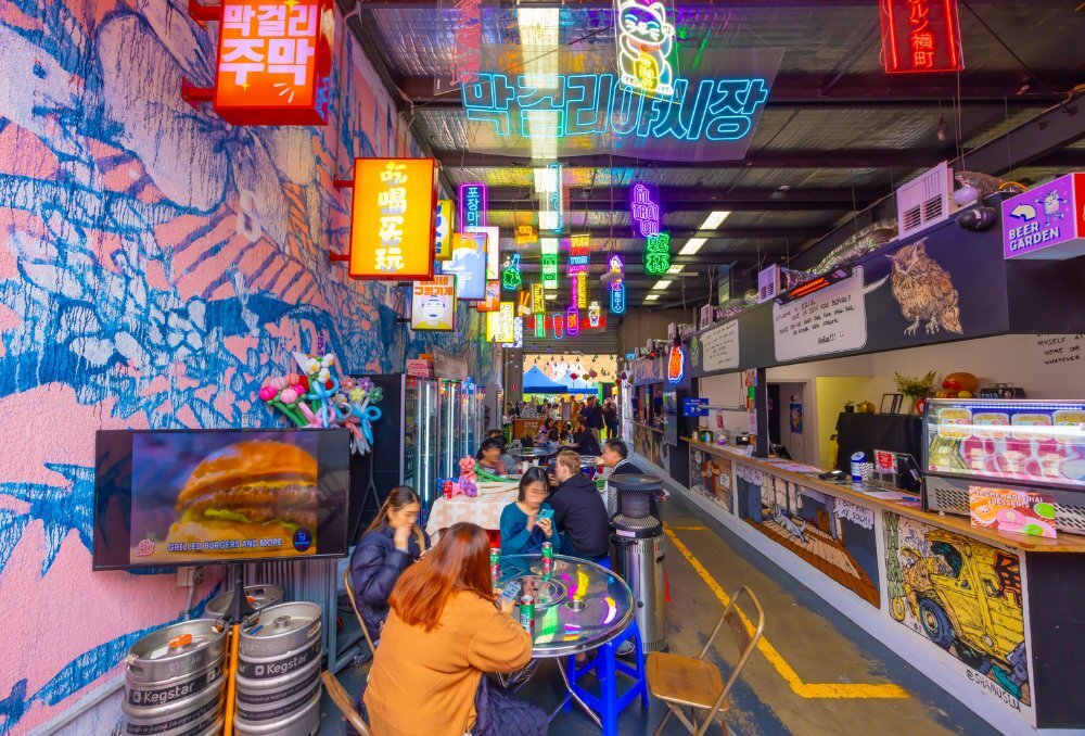 Colourful dining hall with groups of patrons eating around round tables.