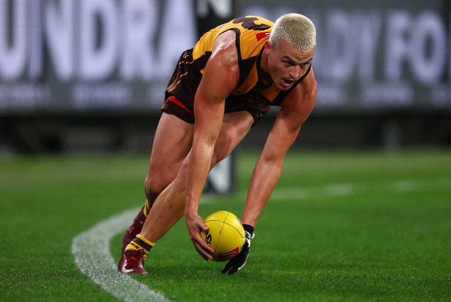A Hawthorn AFL football player picking up a ball on the field during a match.