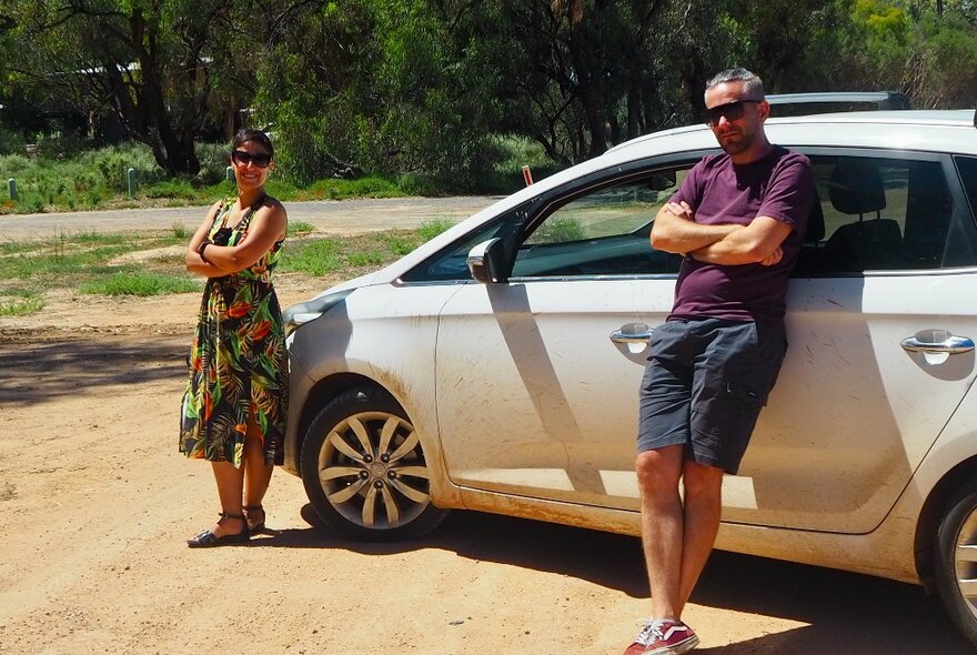 A man and a woman leaning against a car at a roadside stop in the country.