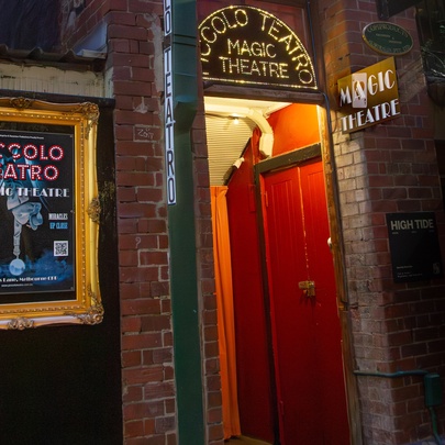 The hidden entrance to Piccolo Teatro with a red door and lit up signage above.