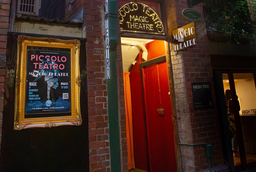 The hidden entrance to Piccolo Teatro with a red door and lit up signage above.