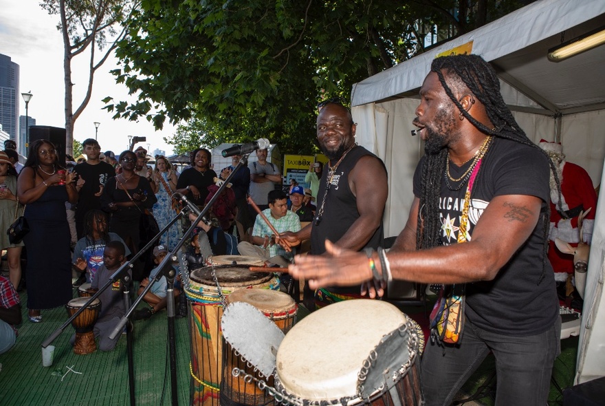 An African drumming group performing outdoors to a small group of people. 