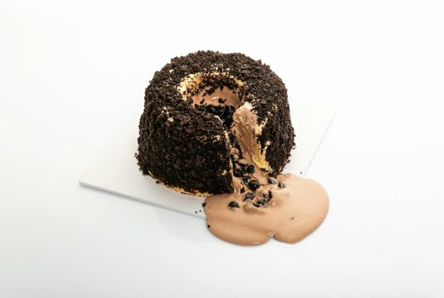 A round cake iced with chocolate sprinkles, sliced and oozing chocolate cream.