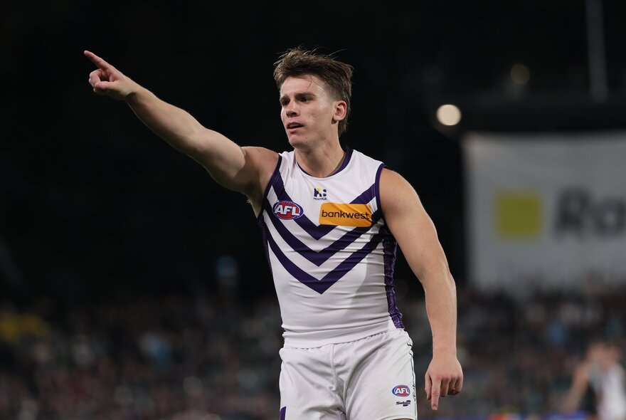 A Fremantle AFL player with his arm raised above him, pointing in victory at the goals.