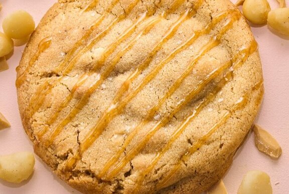 Close up of caramel macadamia nut cookie, drizzled with syrup.
