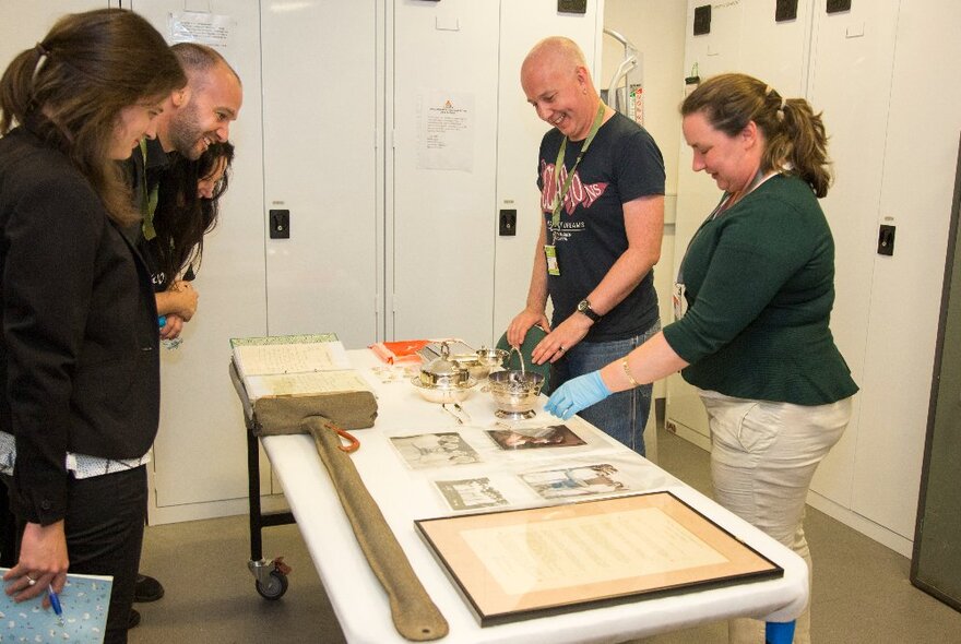 Museum curators showing a group of people a collection of artefacts on a white table.