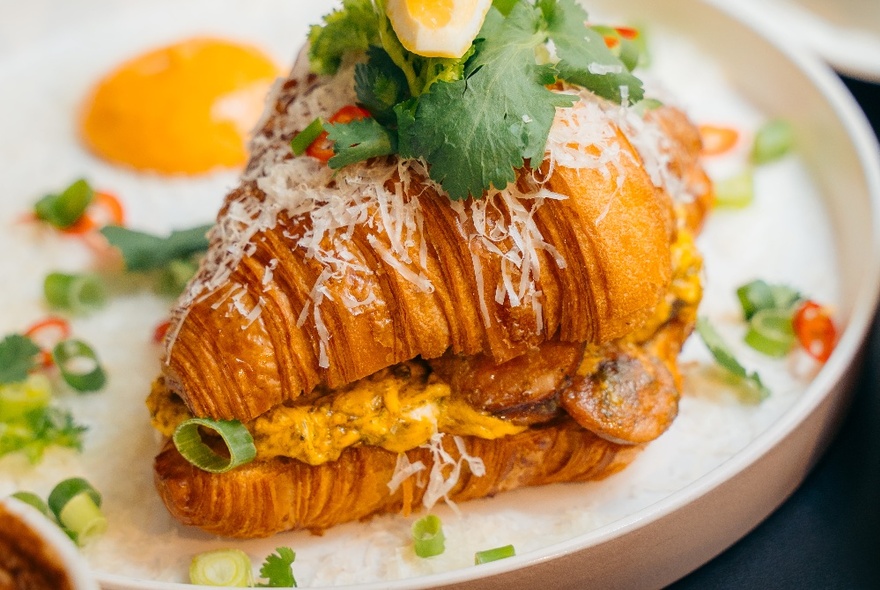 A filled croissant halved topped with salad and eggs.