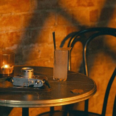 A small table for one with a sunset glow on the wall, a tall drink with a straw on the table and a votive candle.