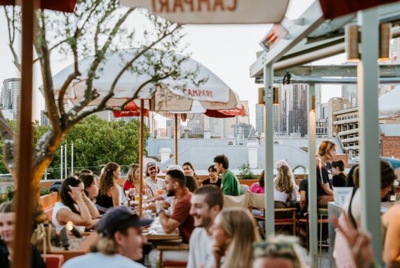 People drinking and dining in an outdoor rooftop courtyard.