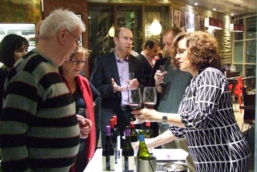 A wine tasting with people mingling a woman passing out samples of wine in glasses. 