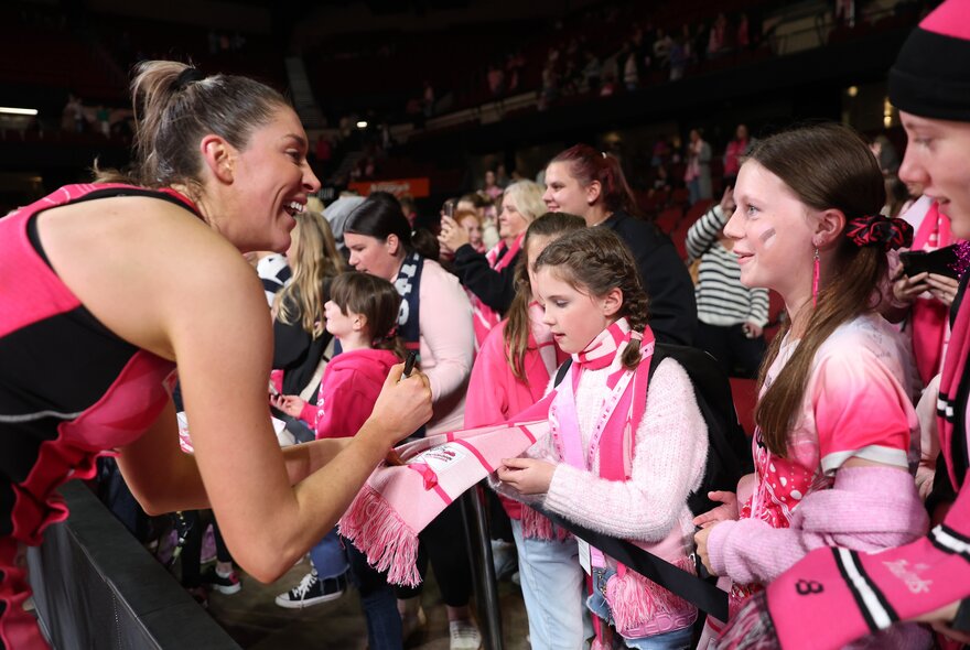 Netball player signing autographs for young fans wearing team colours.