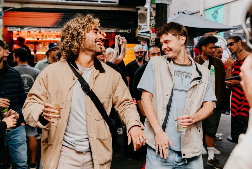 Two young men celebrating at a bar in Melbourne, both smiling and dancing.