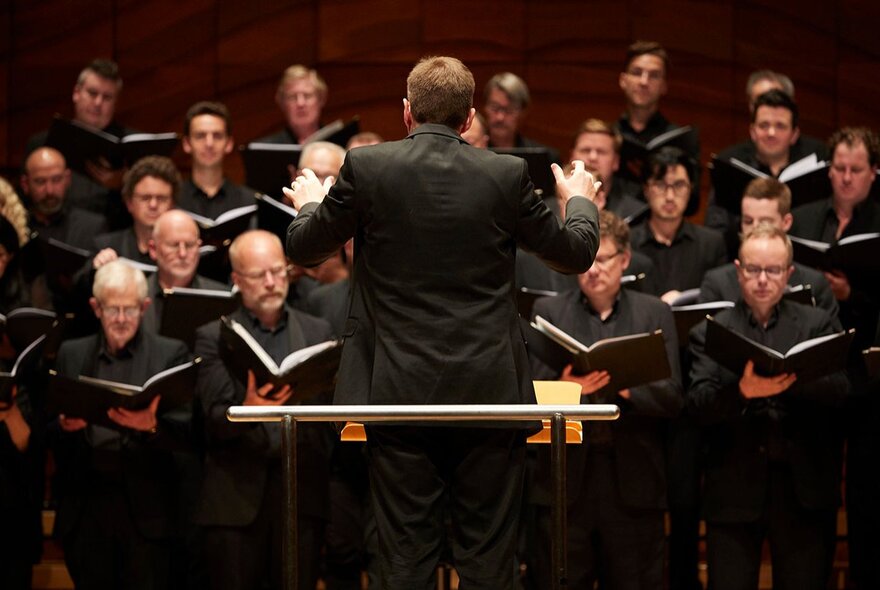 The back of a conductor as he conducts a choir in a concert hall. 