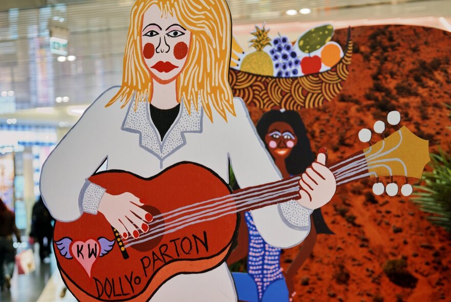 A pop-up installation featuring a cardboard Dolly Parton with her guitar and exaggerated red cheeks. 