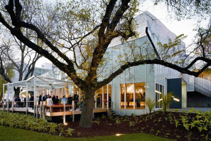 A wedding venue at dusk with glowing lighting and large tree.