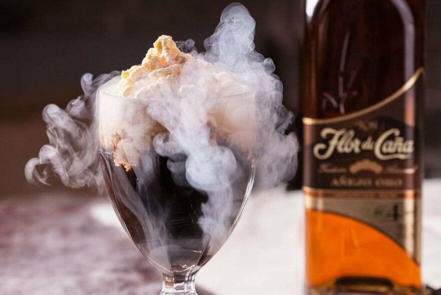 A cocktail with whipped cream and nitro smoke on top.