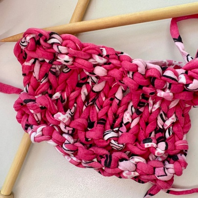 A knitting project being worked on with bright pink and variegated t-shirt yarn using wooden knitting needles.