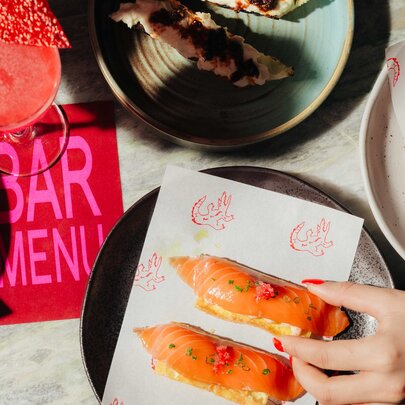 Hands reaching for food from a plate with bar menu.