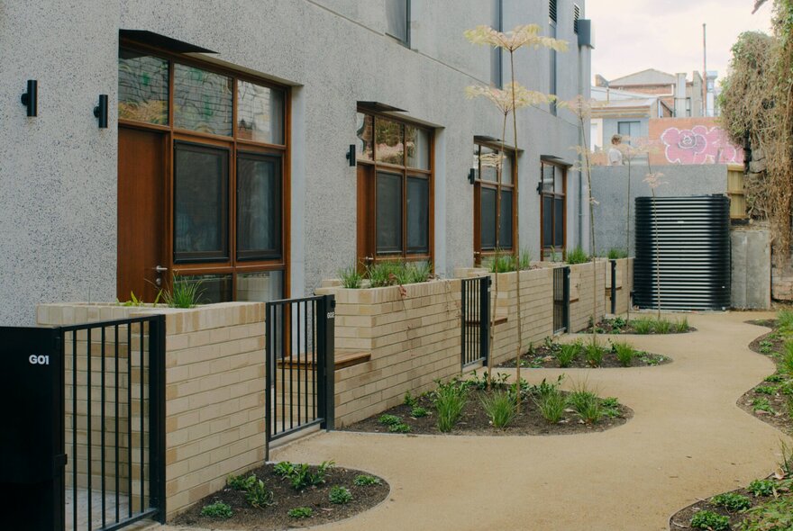 An outdoor walkway runs alongside a modern, multi-story building featuring light grey walls and large, dark-framed windows with wooden accents.