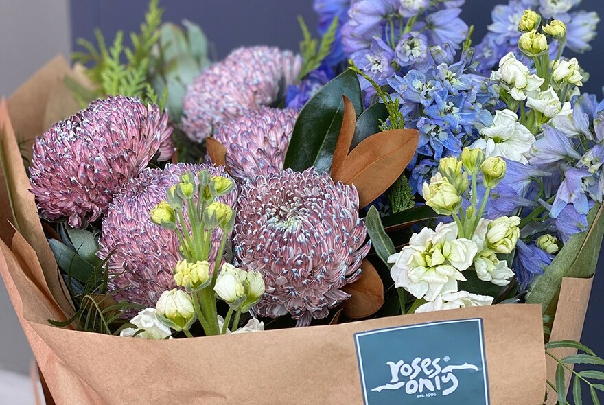 A bouquet of purple and blue flowers wrapped in brown paper.