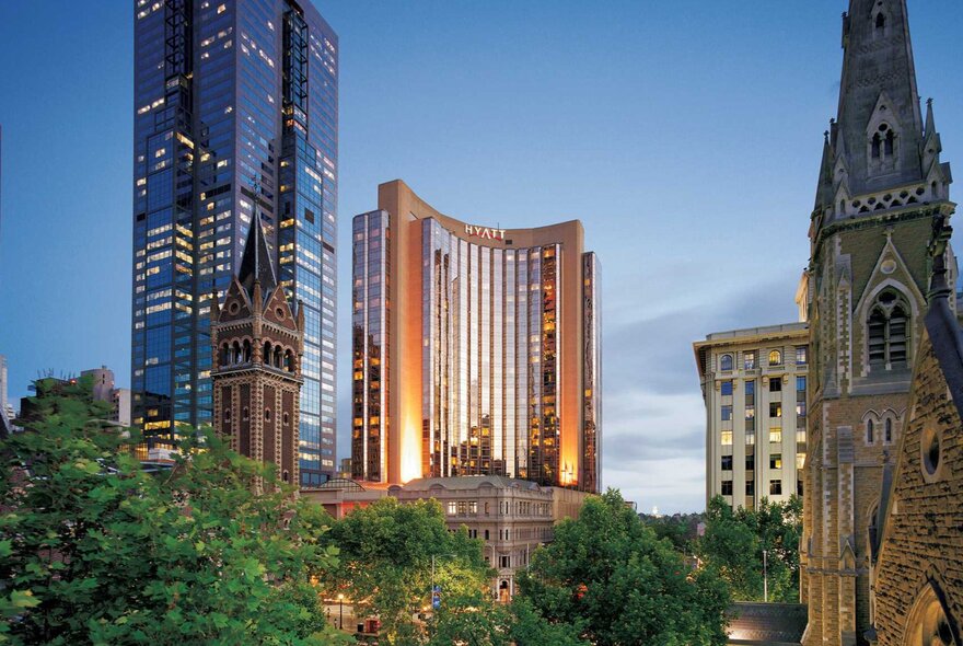 A view of the Melbourne skyline at dusk, showing the Grand Hyatt Melbourne with peachy lights and a cathedral spire on the right. 