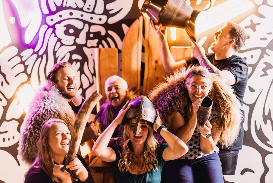 People having a fun time dressed in furs and hats as vikings, with viking murals behind them. 