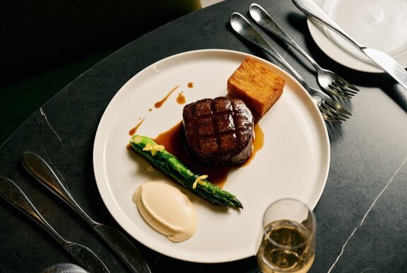 Meat and aspagarus on a plate with cutlery and glass of white wine.