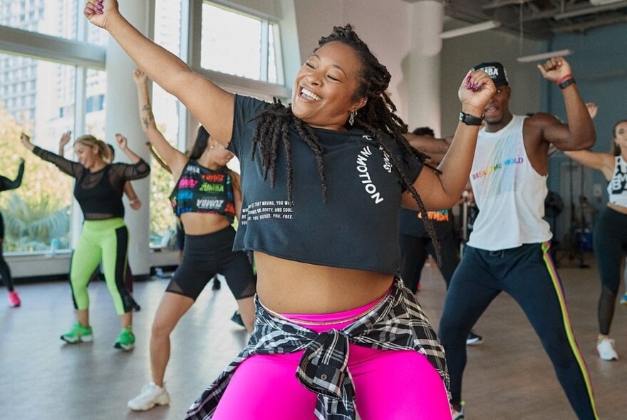 A woman looking strong and confident while she does a group activity class in bright pink pants. 