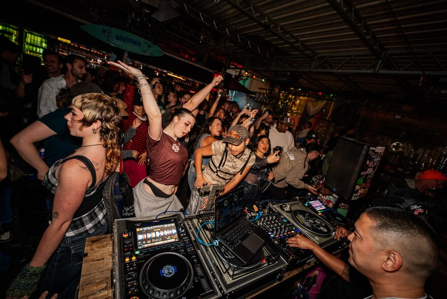 A lively crowd dancing at Section 8 Bar, with a DJ at the turntable mixing desk.